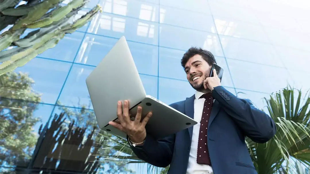 Homem segurando um notebook com uma mão e conversando ao celular