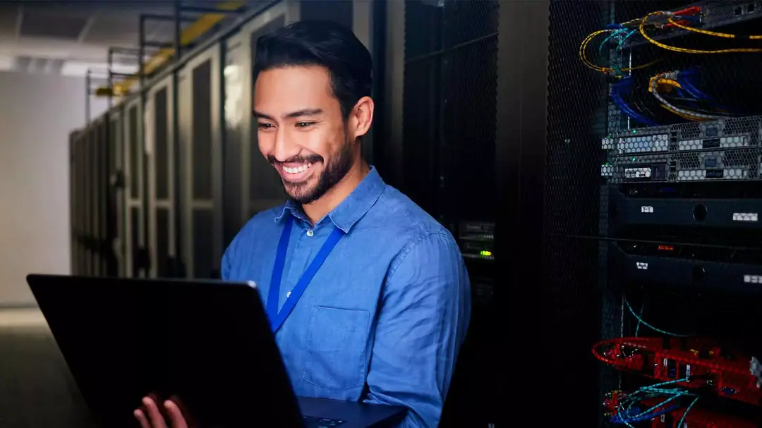 Homem sorrindo segurando um computador portátil em um data center