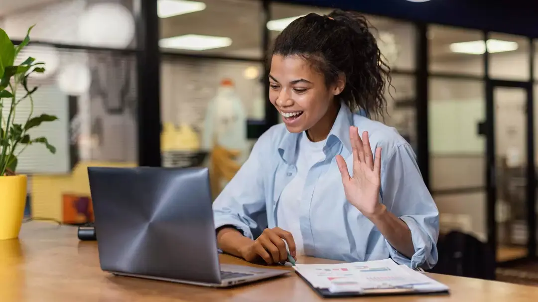 Mulher sorrindo e acenando durante uma chamada de vídeo no notebook