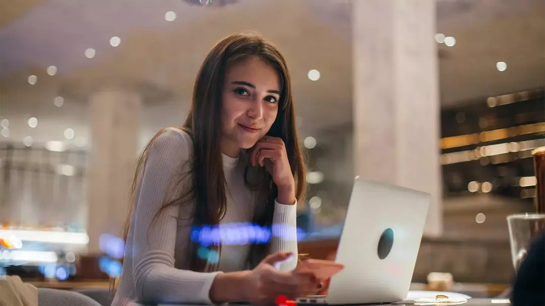 Mulher sentada segurando um celular e com um notebook à sua frente