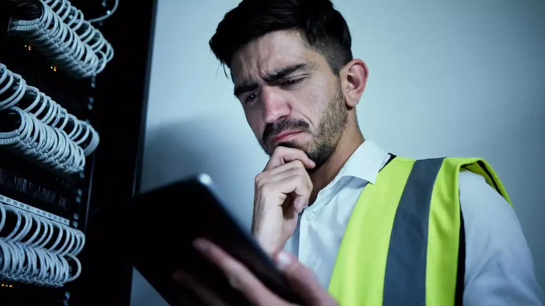 Homem analisando dados em um tablet diante de um rack de rede